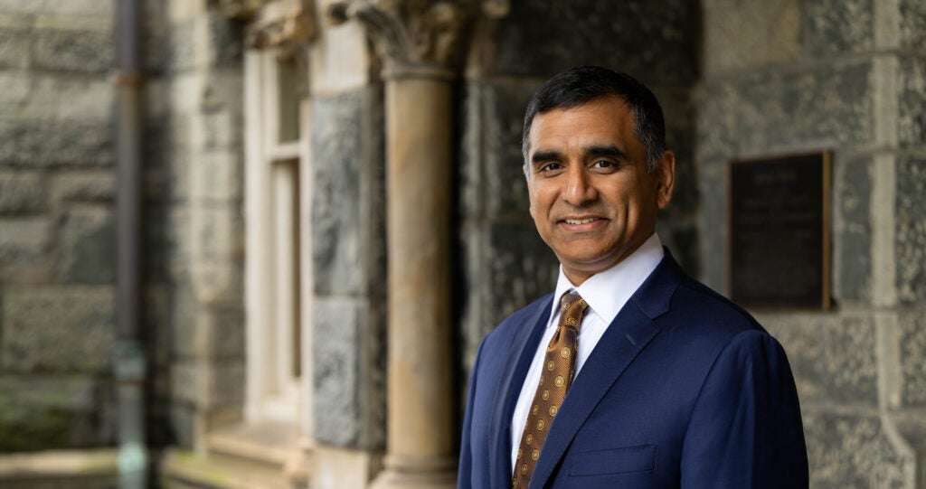 headshot of Hari Sastry, CFO, in front of a stone building called Healy Hall. Hari is wearing a suit and tie.